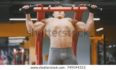 Muscular young man pulling up in a gym, close up