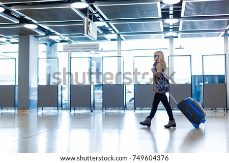 Beautiful indian tourist walking in the airport hall while wearing winter clothes and carrying 