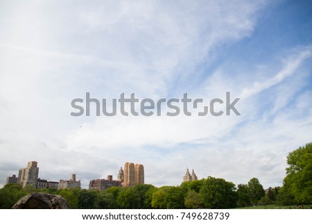 Buildings and cloudy sky behind trees at Central Park in spring