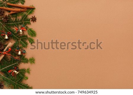 Christmas decoration, cinnamon sticks, small bells and garland frame, copy space on craft paper background. Xmas ornaments border with fir tree branches