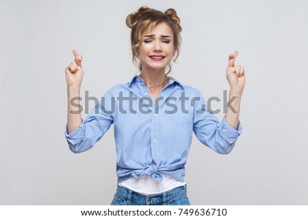 Human emotions and feelings. Superstitious teenager girl with blonde hair and pretty face crossing fingers for good luck, hoping her wishes will come true, having excited happy look. 