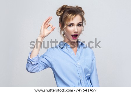 Happiness woman with charming smile making ok gesture being agreeable. Cute smiling female with blonde hair showing okay sign. Studio shot on gray background