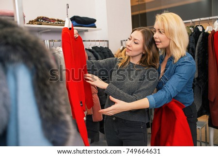 Two attractive women looking at red sweater in shopping mall. Shopping concept