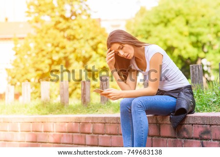 A young woman receiving bad news using a app on her smartphone in a park.
