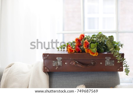 a bouquet of orange roses on a vintage leather suitcase, in a room near the window