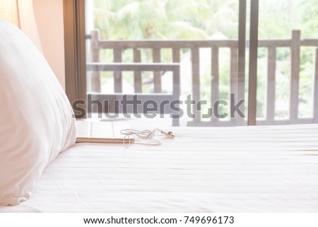close up of white bed with pillow and blanket laptops with earphone on bed and blur garden view balcony, shallow depth of field