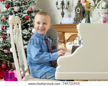 Elegant little boy in shirt and tie playing on a white Grand piano. Around the Christmas tree and the fireplace in the Christmas night.