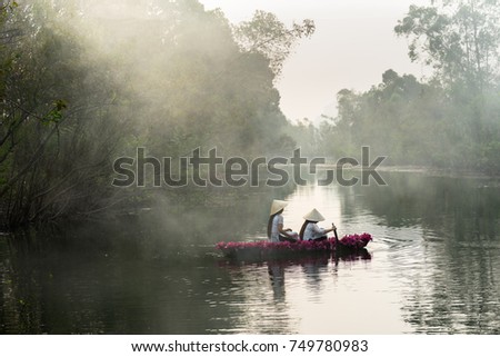 River scene with smoke, a boat carrying girls wearing traditional dress Ao Dai, conical hat, and flower.
