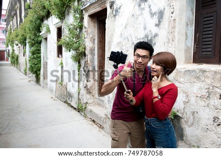 Asian couple traveler taking selfie photo with selfie stick with vintage town in background.