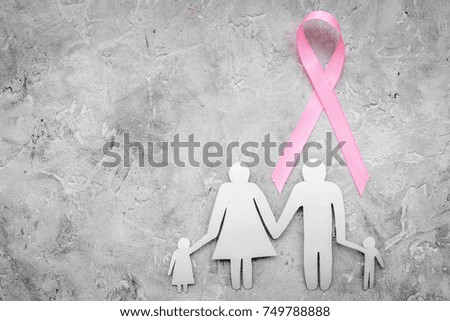 Hand hold pink ribbon for breast cancer awareness near paper silhouette of family on grey stone background top view copyspace
