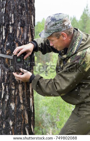 Camera traps with infrared light and a motion detector attached by straps on a tree  in the Siberian taiga.
Foresters install photo traps on a tree for automatic photographing or video shooting of wil