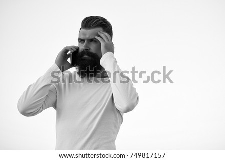 One handsome young bearded serious business man in white sweater holding and speaking on cell phone outdoor on light sky natural background, horizontal picture