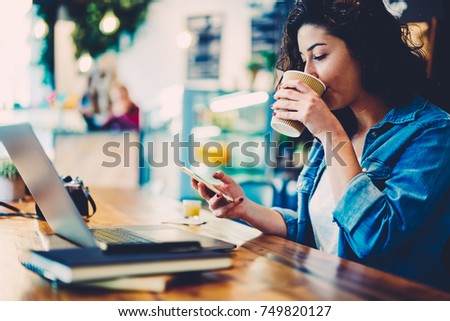 Young female person enjoying takeaway coffee while sharing news and chatting with followers via smartphone and internet connection.Cropped image of hipster girl drinking beverage and checking email