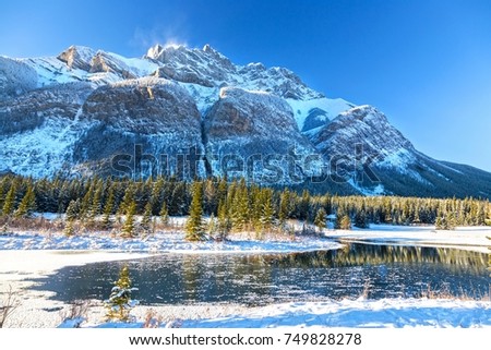 Snowcapped Cascade Mountain and Freezing Lake Landscape on Cold Day after early Autumn Snowfall in Banff National Park