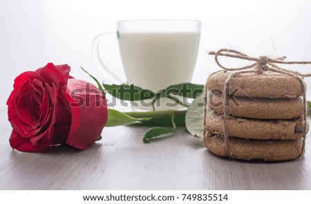 Transparent cup of milk, stack of cookies, perevyazanaya twine, lies next to a red rose. Blurred background, bokeh. Romantic picture, breakfast. Festive mood. Beautiful background.