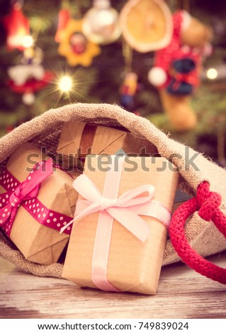 Vintage photo, Wrapped gifts with ribbons in jute sack for Christmas and christmas tree with lights and decoration in background, festive time concept