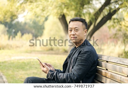Asian middle-aged men in the autumn park, watching cell phones, smiling