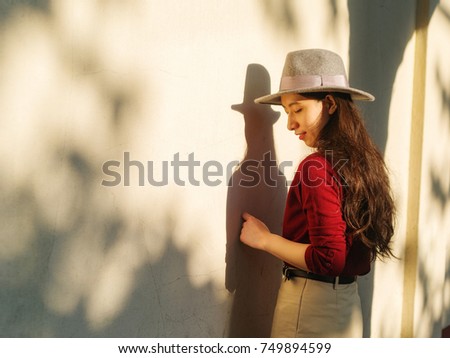 Pretty Chinese young woman stand in warm sunshine with shadows on wall.