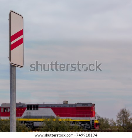 Road sign Approaching the railway crossing against the background of a passing red train in the evening