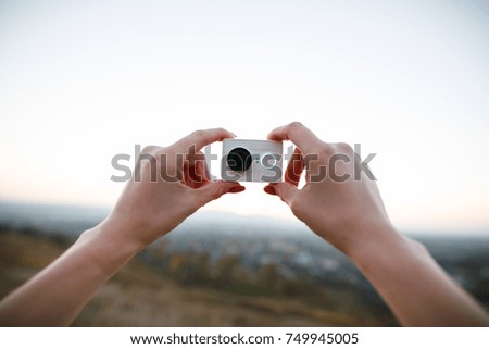 human hands holding an action camera on the sunset background