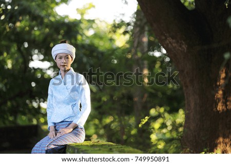 Portrait of thai young woman with traditional thai dress sit in thai temple with tree and sunrise