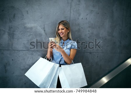Young woman holding shopping bags and using her phone