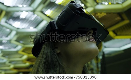Close up of a young woman in VR glasses. She is amazed by what she is seeing. She is standing against an abstract background