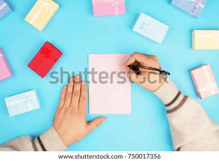 Top view of hands holding a small box with a gift and a ribbon on a blue background.