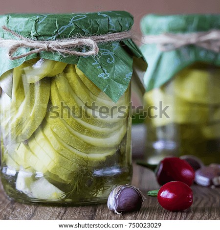 Pickled zucchini in glass jar on a brown wooden table. Soft focus.
