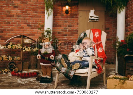 Playful happy cute little child boy dressed in a sweater and jeans sitting on the chair with Santa in decorated New Year room at home. Christmas good mood. Lifestyle, family and holiday 2018 concept