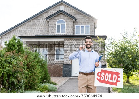 handsome smiling realtor with keys of sold house