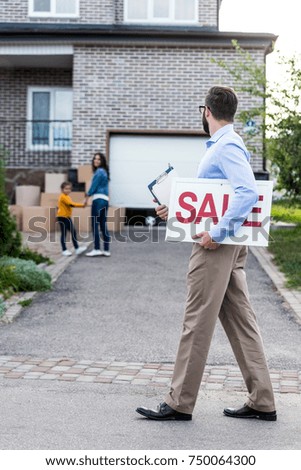 realtor with sale sign walking in front of people moving into new house