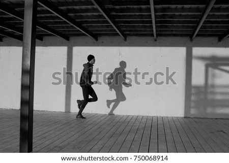black and white picture of male runner training, shadow of runner on white wall 