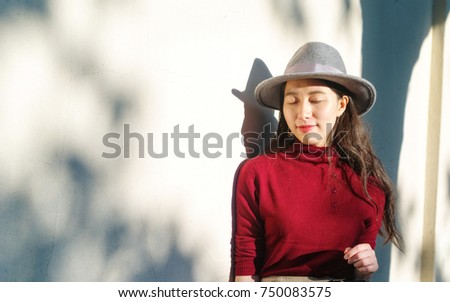 Pretty Chinese young woman stand in warm sunshine with shadows on wall.