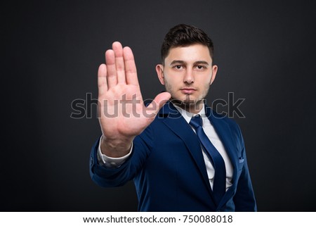 Attractive businessman rising his palm up and doing stop gesture on dark background