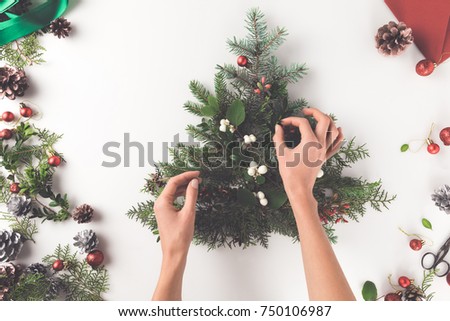 cropped view of hand making christmas tree from fir branches, christmas balls, mistletoe and pine cones, isolated on white