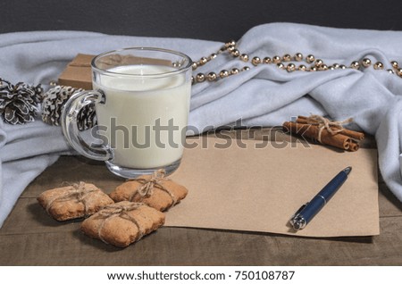 A cup of milk, cinnamon sticks, homemade cookies and a sheet of paper with a pen in a Christmas decor.