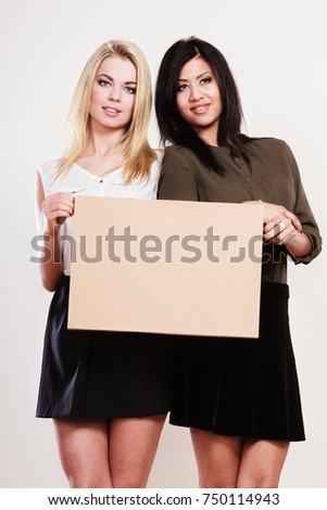 Advertisement concept. Two women caucasian and african with blank board empty banner cardboard studio shot