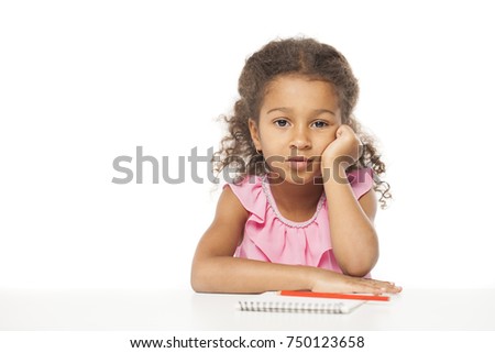 Education. Close up portrait of african little girl is sitting at the table with a notebook for drawing, isolated on white background