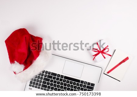 Workspace with laptop and christmas gift and santa hat on white background flat lay, top view, copy space.  Business christmas holidays concept, holiday online shopping