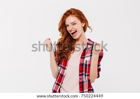 Picture of excited beautiful young redhead lady standing isolated over white wall background showing winner gesture.