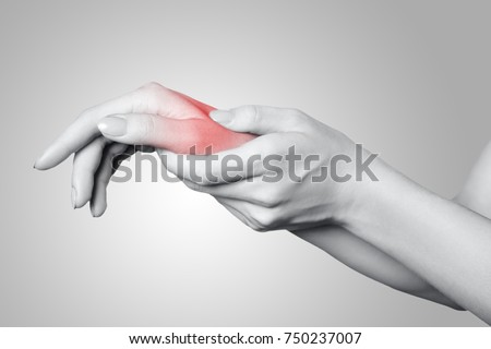 Closeup view of a young woman with pain on hand on gray background. Black and white photo with red dot.