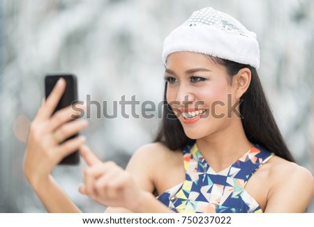 Beautiful toothy smiling young woman in white santa's hat  taking a selfie against blur background.Christmas selfie concept.