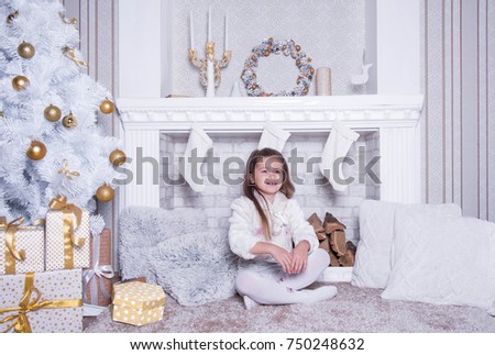 Funny girl in Christmas living room. Girl with gifts at the fireplace.  Portrait with copy space. White beautiful decor. 