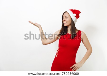 Beautiful caucasian happy woman with charming smile wearing red dress and Christmas hat looking away, holding copy space on palm isolated on white background. Santa girl. New Year holiday 2018