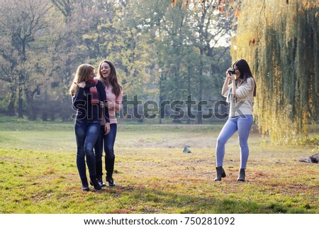 Three girls havin fun in park, one of them have old film camera and taking pictures of two young long hair girls who posing