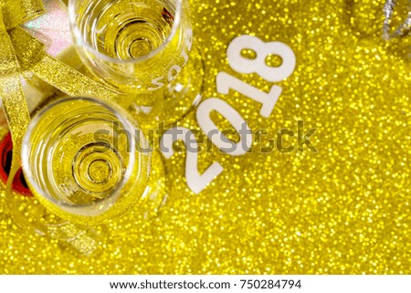 Glass of white wine, combined with a gift box and shining balls on a bright gold floor. Focus at wine in glass. Shallow depth of field. There is texts "2018" blurred on background