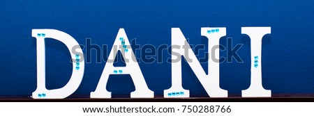 Word dani written in Spanish, made with white wood on a blue background