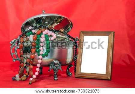 empty wooden photo frame is standing next to a casket of jewels on a background of red fabric. can used for display or montage of your products as well as greeting card in retro style