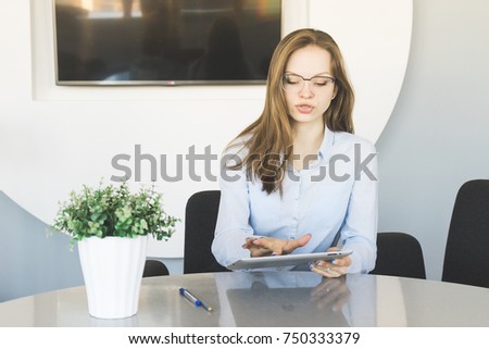 stylish successful girl in glasses and blue shirt is working in the office, looking at the tablet